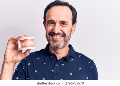 Middle age handsome man holding denture showing teeth over isolated white background looking positive and happy standing and smiling with a confident smile showing teeth - Powered by Shutterstock