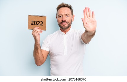 Middle Age Handsome Man Looking Serious Showing Open Palm Making Stop Gesture. 2022 Calendar Concept