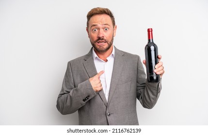 Middle Age Handsome Man Looking Shocked And Surprised With Mouth Wide Open, Pointing To Self. Wine Bottle Concept