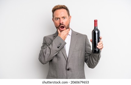 Middle Age Handsome Man With Mouth And Eyes Wide Open And Hand On Chin. Wine Bottle Concept