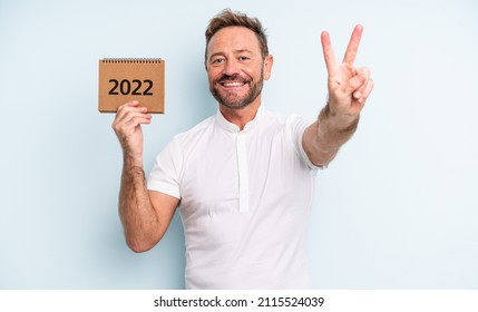 Middle Age Handsome Man Smiling And Looking Happy, Gesturing Victory Or Peace. 2022 Calendar Concept