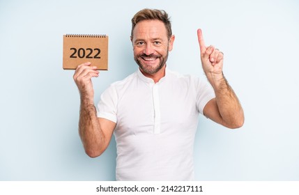 Middle Age Handsome Man Smiling And Looking Friendly, Showing Number One. 2022 Calendar Concept