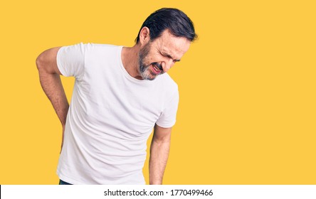 Middle age handsome man wearing casual t-shirt suffering of backache, touching back with hand, muscular pain 