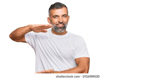 Middle Age Handsome Man Wearing Casual White Tshirt Gesturing With Hands Showing Big And Large Size Sign, Measure Symbol. Smiling Looking At The Camera. Measuring Concept. 