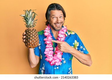 Middle Age Handsome Man Wearing Hawaiian Lei Holding Pineapple Smiling Happy Pointing With Hand And Finger 