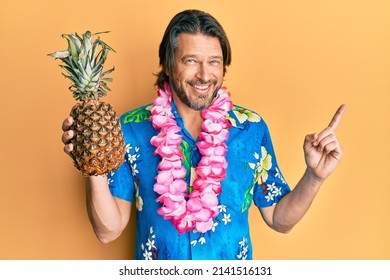 Middle Age Handsome Man Wearing Hawaiian Lei Holding Pineapple Smiling Happy Pointing With Hand And Finger To The Side 