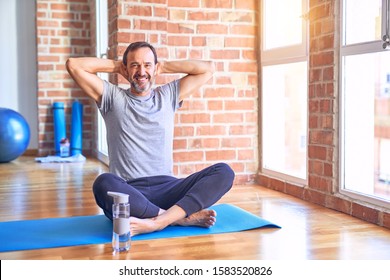 Middle age handsome sportman sitting on mat doing stretching yoga exercise at gym relaxing and stretching, arms and hands behind head and neck smiling happy - Powered by Shutterstock