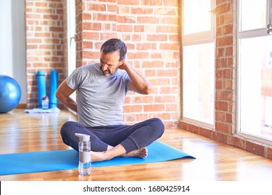 Middle age handsome sportman sitting on mat doing stretching yoga exercise at gym Suffering of neck ache injury, touching neck with hand, muscular pain - Powered by Shutterstock