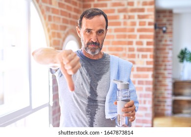 Middle Age Handsome Sportman Sweaty Holding Bottle Of Water And Towel After Exercise At Gym With Angry Face, Negative Sign Showing Dislike With Thumbs Down, Rejection Concept