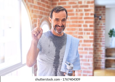 Middle Age Handsome Sportman Sweaty Holding Bottle Of Water And Towel After Exercise At Gym Surprised With An Idea Or Question Pointing Finger With Happy Face, Number One