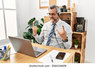 Middle Age Hispanic Business Man Working At The Office Wearing Operator Headset Shouting With Crazy Expression Doing Rock Symbol With Hands Up. Music Star. Heavy Concept. 