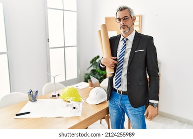 Middle age hispanic business man holding paper blueprints relaxed with serious expression on face. simple and natural looking at the camera. 