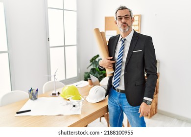 Middle age hispanic business man holding paper blueprints looking at the camera blowing a kiss on air being lovely and sexy. love expression. 