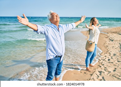 Middle age hispanic couple breathing with arms raised at the beach. - Powered by Shutterstock