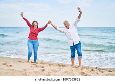 Middle age hispanic couple breathing with arms raised at the beach. - Powered by Shutterstock