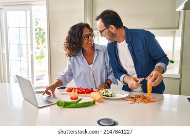 Middle Age Hispanic Couple Cooking And Using Laptop At Kitchen