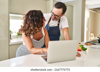 Middle Age Hispanic Couple Cooking And Using Laptop At Kitchen