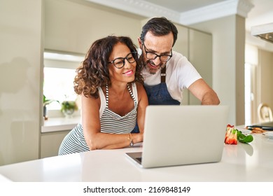 Middle Age Hispanic Couple Cooking And Using Laptop At Kitchen