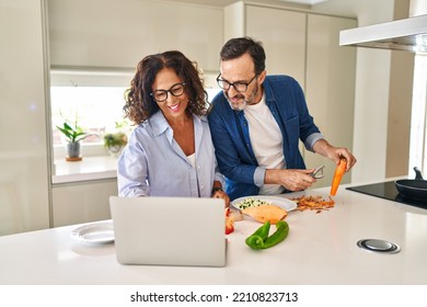 Middle Age Hispanic Couple Cooking And Using Laptop At Kitchen