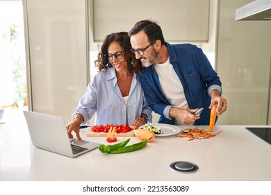 Middle Age Hispanic Couple Cooking And Using Laptop At Kitchen