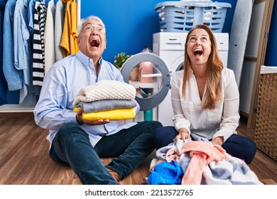 Middle Age Hispanic Couple Doing Laundry Sitting On The Floor Angry And Mad Screaming Frustrated And Furious, Shouting With Anger Looking Up. 