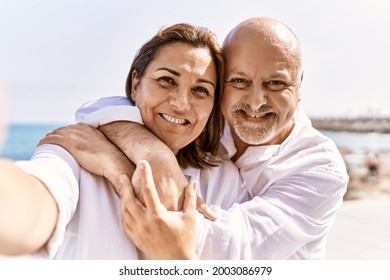 Middle age hispanic couple of husband and wife together walking by the beach on a sunny day. Hugging in love on vacation to the seaside taking a selfie picture - Powered by Shutterstock