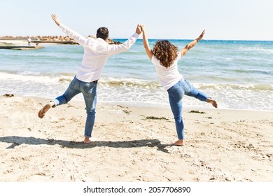 Middle Age Hispanic Couple On Back View Dancing At The Beach.