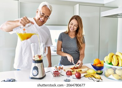 Middle age hispanic couple pouring juice on mixer machine cooking smoothie at the kitchen. - Powered by Shutterstock