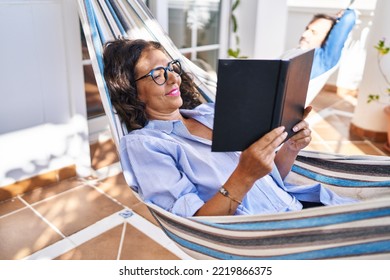 Middle age hispanic couple reading book lying on hammock at terrace - Powered by Shutterstock