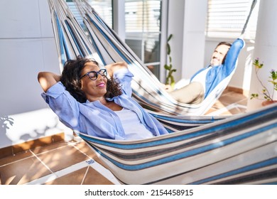 Middle age hispanic couple relaxed with hands on head lying on hammock at terrace - Powered by Shutterstock