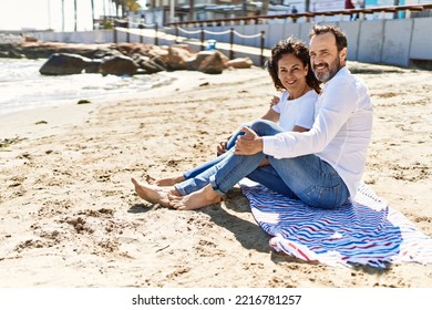 Middle age hispanic couple relaxed sitting on the towel at the beach. - Powered by Shutterstock