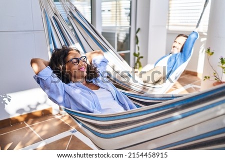 Middle age hispanic couple relaxed with hands on head lying on hammock at terrace