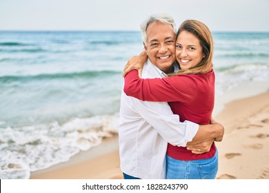 Middle Age Hispanic Couple Smiling Happy And Hugging Walking At The Beach