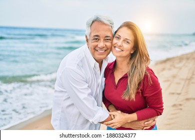 Middle Age Hispanic Couple Smiling Happy And Hugging Walking At The Beach