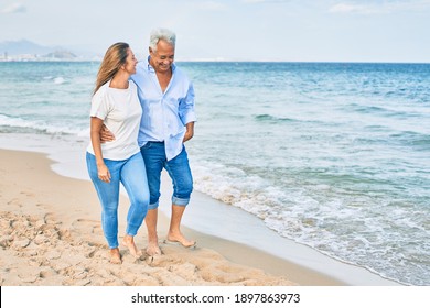 Middle age hispanic couple smiling happy and hugging walking at the beach.