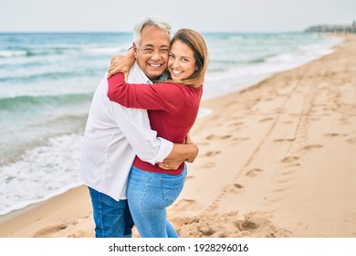 Middle Age Hispanic Couple Smiling Happy And Hugging Walking At The Beach