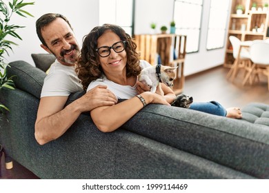 Middle Age Hispanic Couple Smiling Happy Sitting On The Sofa With Dogs At Home.