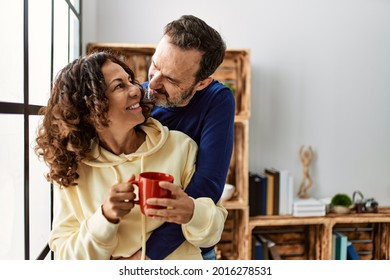 Middle age hispanic couple smiling happy and drinking coffee. Leaning on the window at home. - Powered by Shutterstock