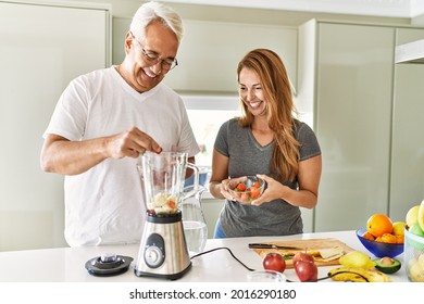 Middle Age Hispanic Couple Smiling Happy Cooking Smoothie At The Kitchen.