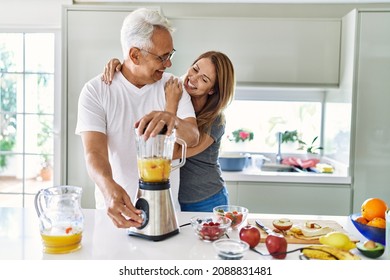 Middle Age Hispanic Couple Smiling Happy And Hugging Cooking Smoothie At The Kitchen.