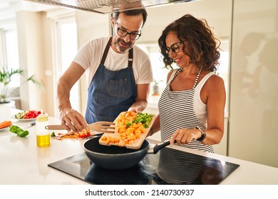 Mittelalter hispanisches Ehepaar lächelt selbstbewusst Essen auf Bratpfanne in der Küche gießen