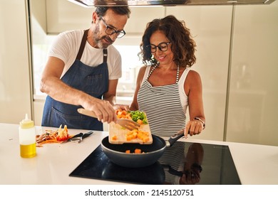 Middle age hispanic couple smiling confident pouring food on frying pan at kitchen - Shutterstock ID 2145120751
