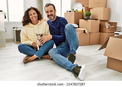 Middle Age Hispanic Couple Smiling Happy Sitting On The Floor With Dog At New Home.