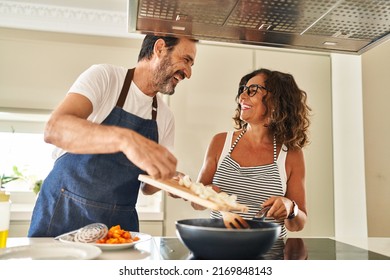 Middle age hispanic couple smiling confident pouring food on frying pan at kitchen - Shutterstock ID 2169848143