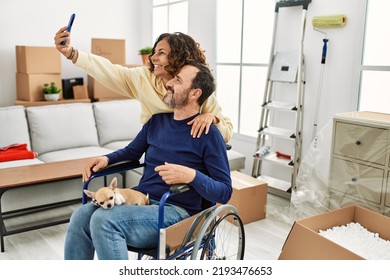 Middle age hispanic couple smiling happy. Man sitting on wheelchair with dog on his legs and woman making selfie by the smartphone at new home. - Powered by Shutterstock