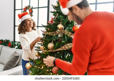 Middle age hispanic couple smiling happy decorating christmas tree at home.