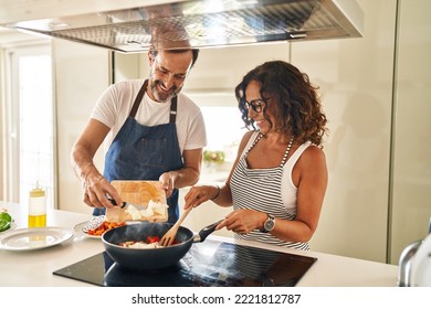 Middle age hispanic couple smiling confident pouring food on frying pan at kitchen - Shutterstock ID 2221812787