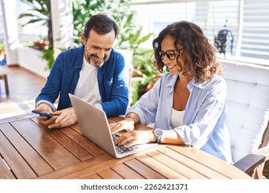 Middle age hispanic couple smiling confident using laptop and smartphone at terrace - Powered by Shutterstock