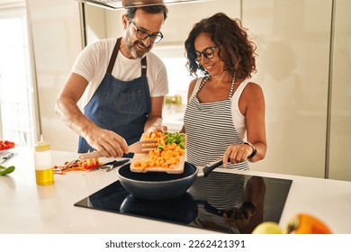 Middle age hispanic couple smiling confident pouring food on frying pan at kitchen - Shutterstock ID 2262421391