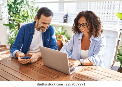 Middle age hispanic couple smiling confident using laptop and smartphone at terrace - Powered by Shutterstock